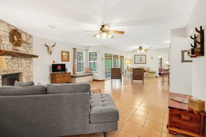 A spacious living room with a grey sectional sofa, a stone fireplace, and a ceiling fan.