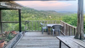 A wooden deck with a table and chairs, overlooking a lush green landscape with hills in the distance.