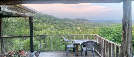 A wooden deck with a table and chairs, overlooking a lush green landscape with hills in the distance.