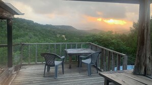 A wooden deck with a table and chairs overlooking a lush valley.