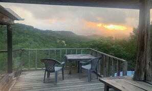 A wooden deck with a table and chairs overlooking a lush valley.