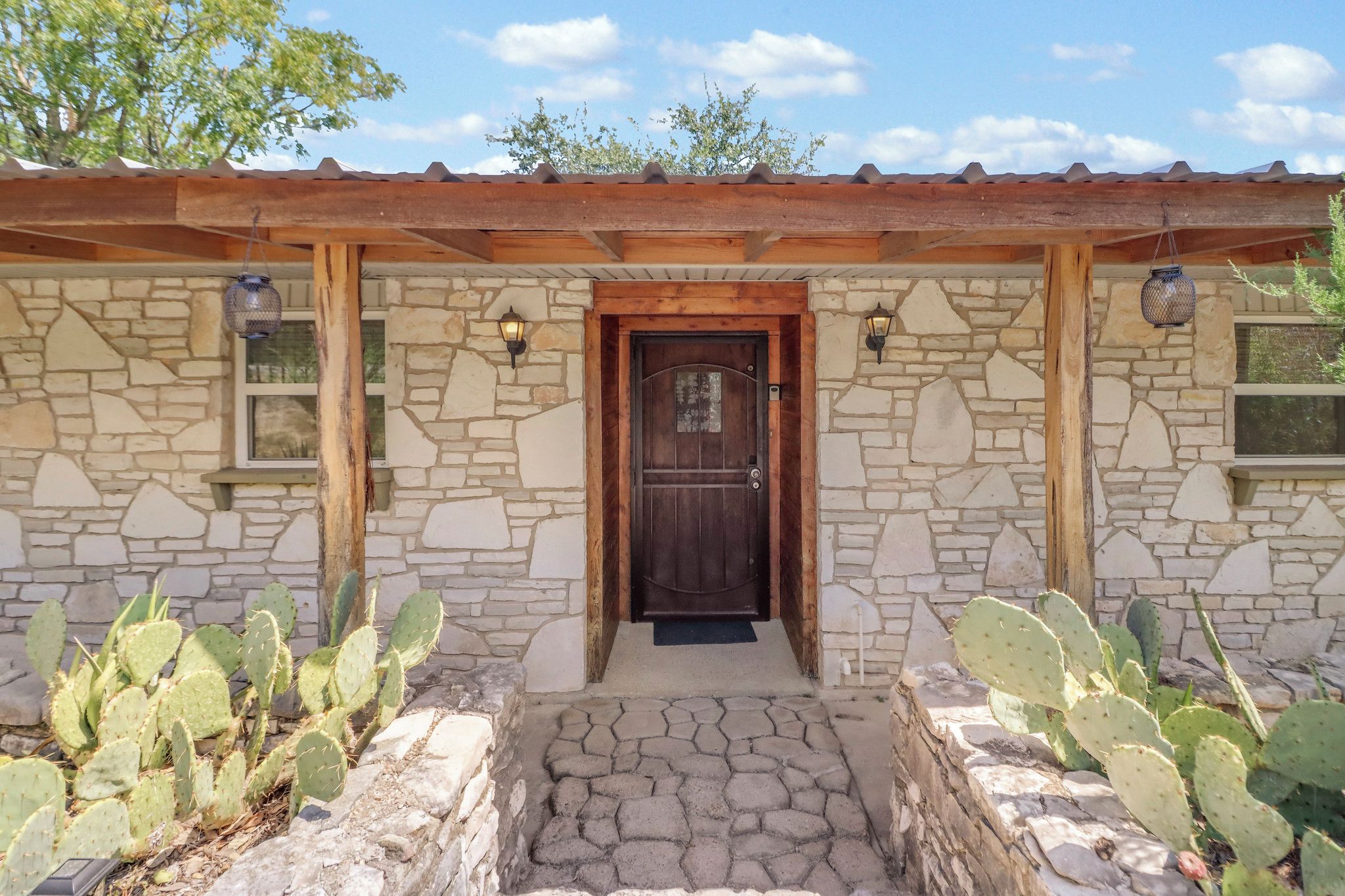 A stone building with a wooden door, two wall-mounted lights, and cacti in front.
