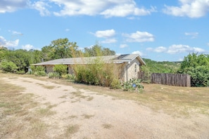 A rustic stone building with a metal roof, surrounded by dry grass and sparse vegetation.