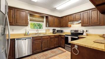 A kitchen with wooden cabinets, stainless steel appliances, a window with a view, and a tiled floor.