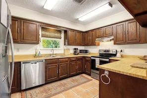 Una cocina con armarios de madera, electrodomésticos de acero inoxidable, ventanal con vistas y piso de baldosas.