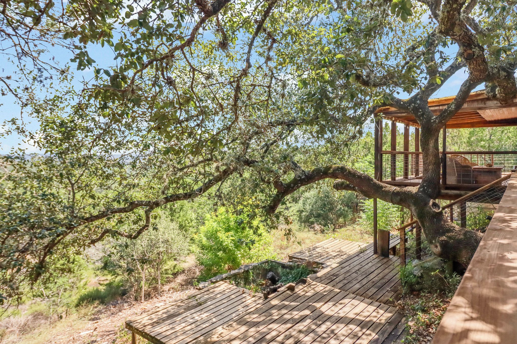 A wooden deck with a gazebo structure, surrounded by trees and greenery.