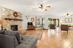 A living room with a stone fireplace, a television, a sofa, and a ceiling fan.