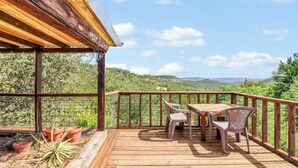 A wooden deck with a table and chairs, overlooking a mountainous landscape.