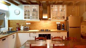 Une cuisine avec des meubles blancs, un plan de travail en bois, une table à manger avec des chaises, une horloge et divers appareils électroménagers.