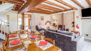 Un coin repas avec une table en bois dressée pour six personnes, un canapé gris et une cheminée en briques.