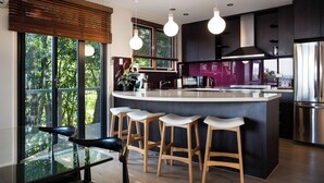 A modern kitchen with a central island, bar stools, and a dining area with a glass table.