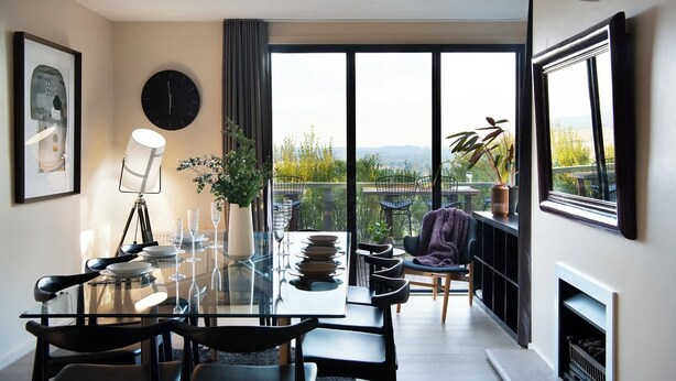 A modern dining area with a glass table, chairs, and a view of the outdoors.