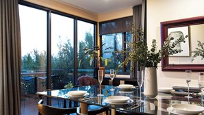 A dining area with a glass table, black chairs, and a view of trees through large windows.