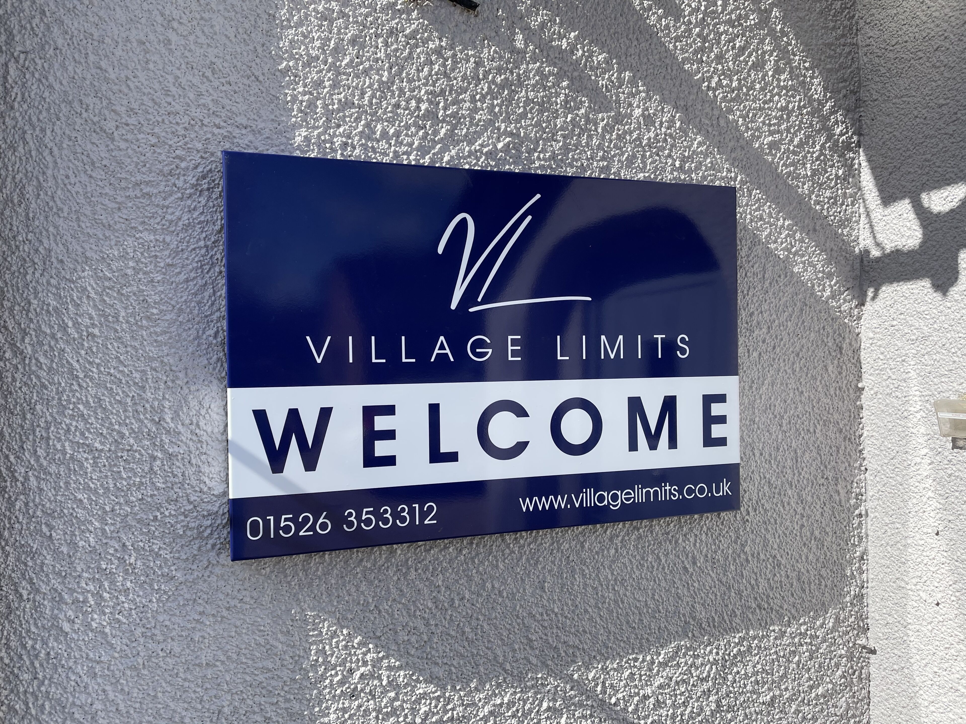 Schild mit der Aufschrift Village Limits, Angabe einer Kontaktnummer und einer Website-URL.