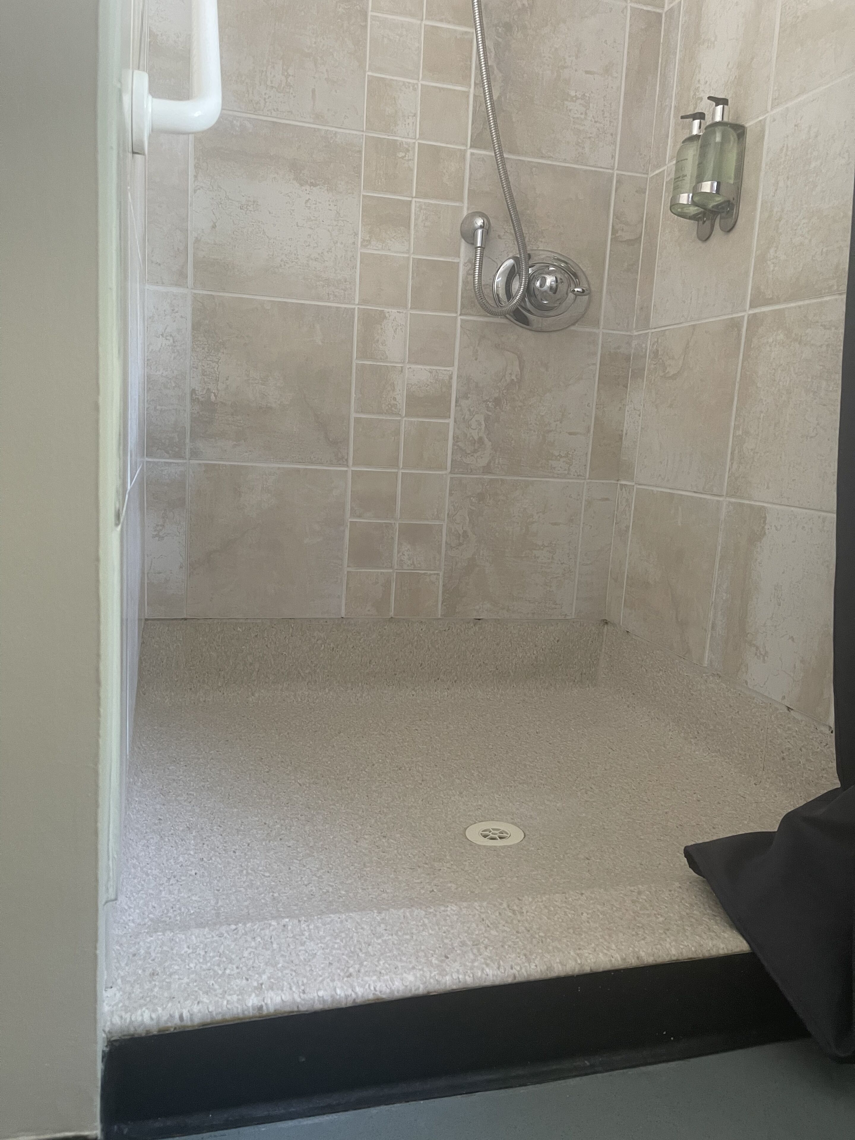 Eine Dusche mit Duschbrause, fest installierter Seifenspender und Ablauf im Boden.