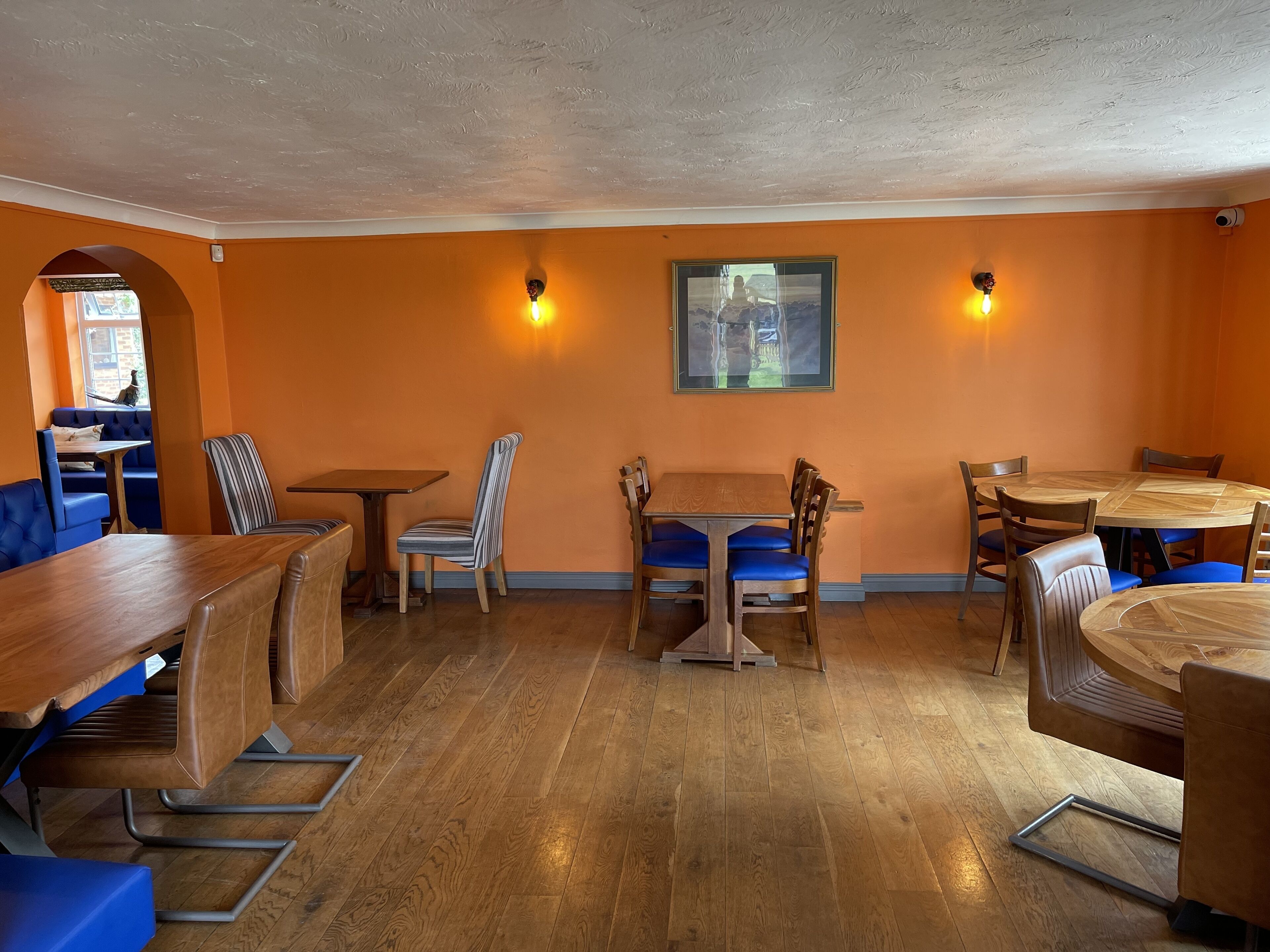 A restaurant interior with wooden tables and chairs, orange walls, and a framed picture on the wall.