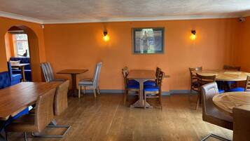 A restaurant interior with wooden tables and chairs, orange walls, and a framed picture on the wall.
