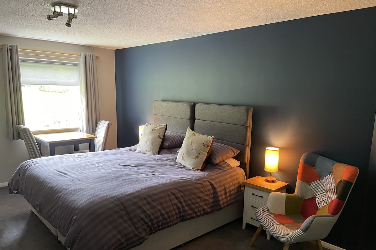 A neatly arranged bedroom with a bed, bedside tables, a chair, and a lamp.