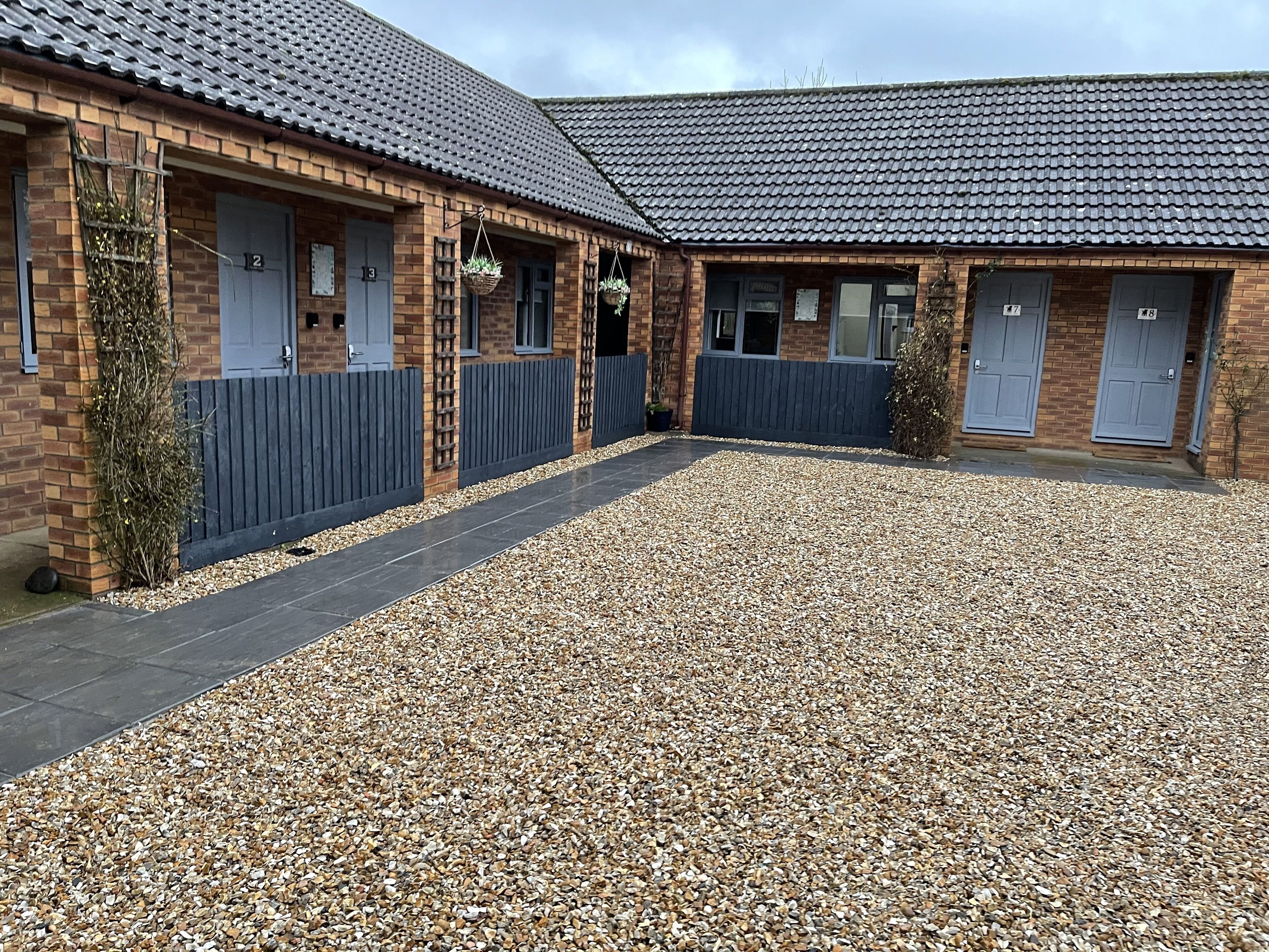 A building with numbered doors, a gravel courtyard, and a tiled roof.