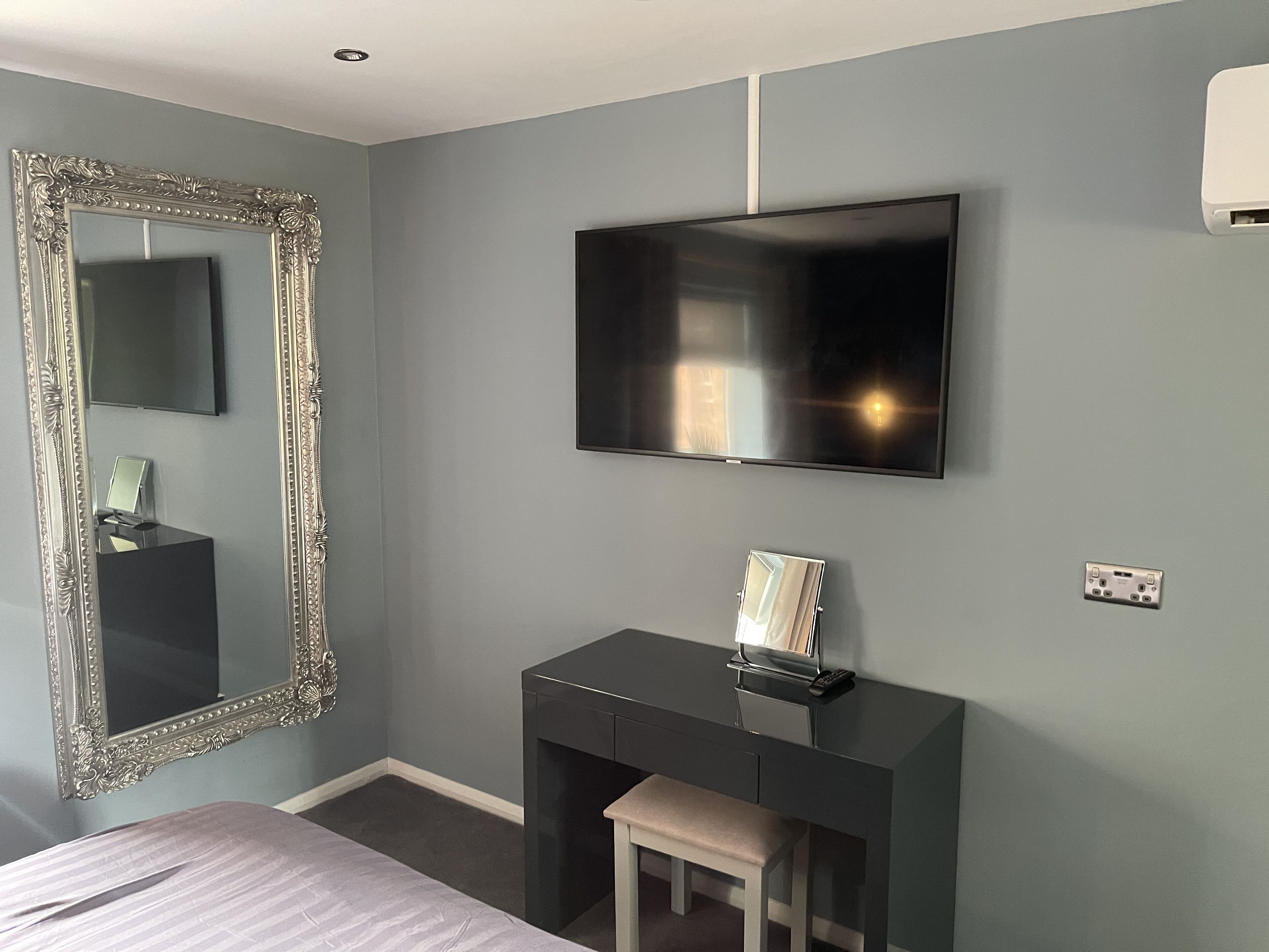 A bedroom with a large mirror, a flat-screen TV, a desk with a chair, and a bed.