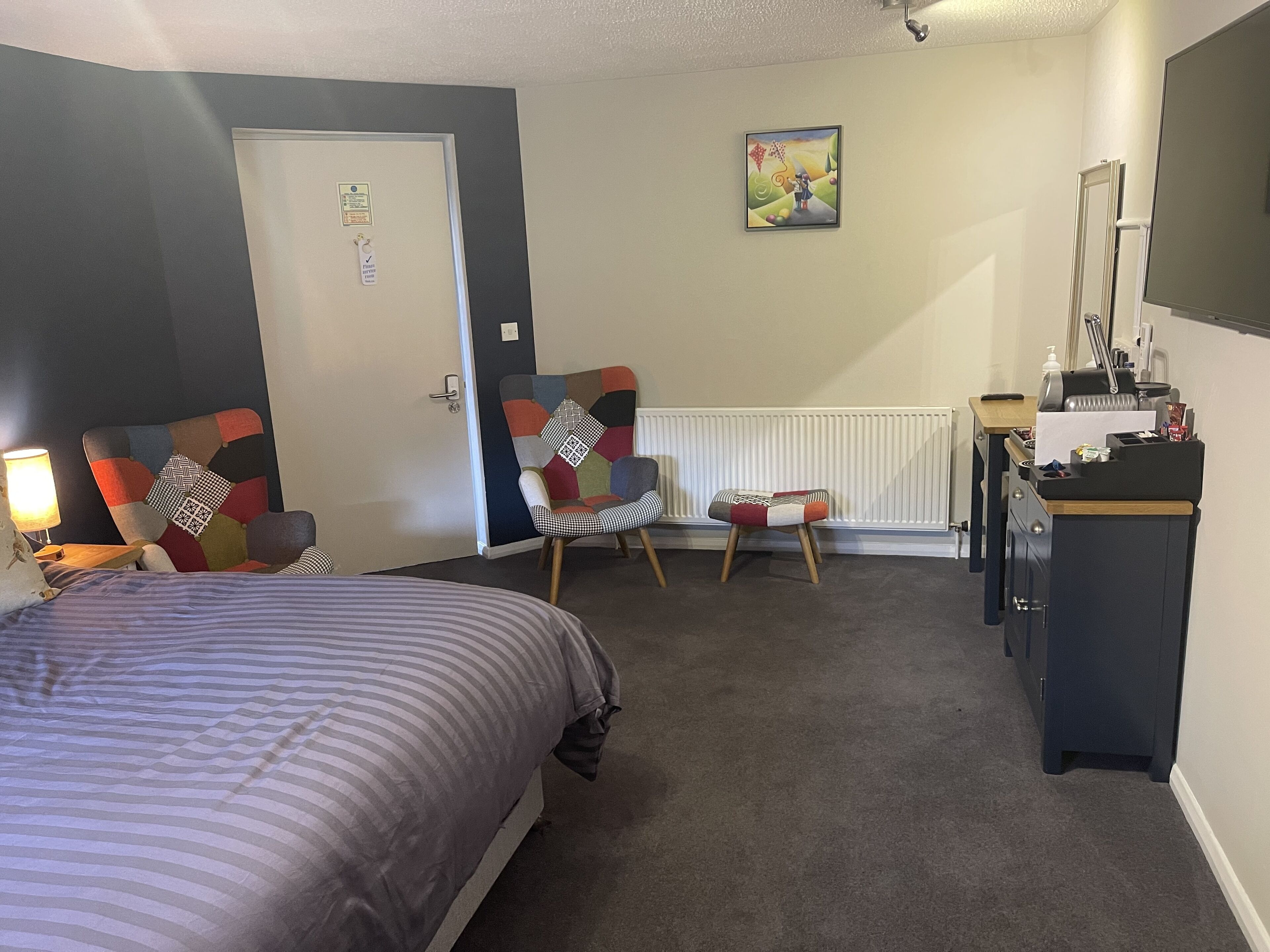 A hotel room with a bed, a chair, a desk, and a radiator.