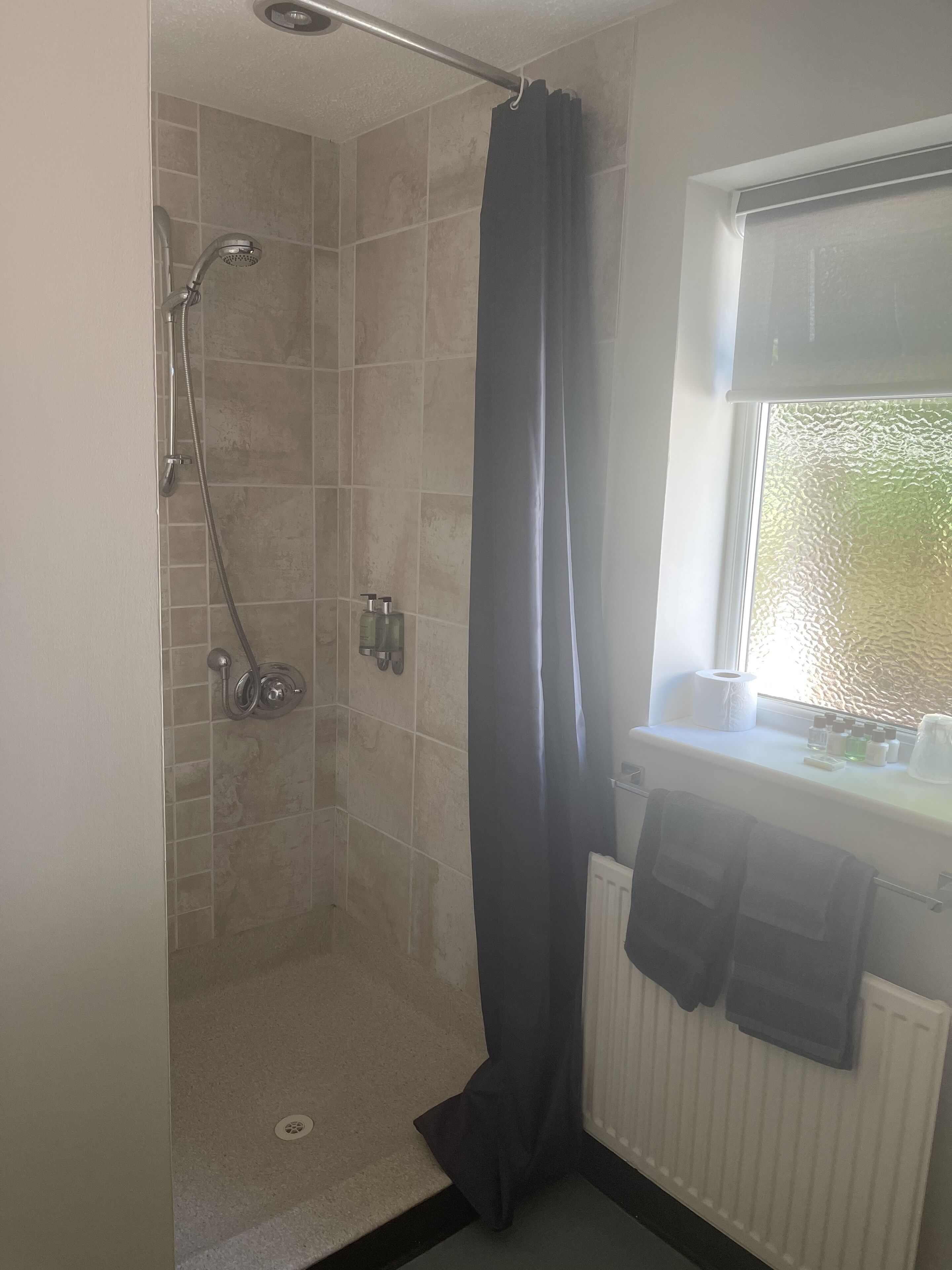 Een douche met een glazen deur, een handdoekrek met handdoeken, en een raam met uitzicht op groen.