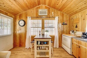 A wooden cabin interior with a kitchen, dining area, and a clock on the wall. - Couples Cabin w/ Luxury Deck, 1 Mi to Canyon Lake! (Canyon Lake)