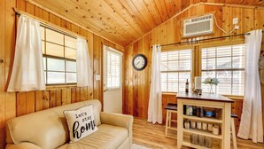 A cozy room with a wooden interior, a leather sofa with a pillow, a wooden table with a vase, and a clock on the wall. - Couples Cabin w/ Luxury Deck, 1 Mi to Canyon Lake! (Canyon Lake)