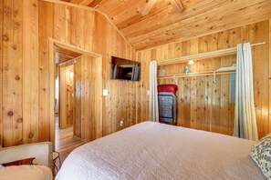 A wooden-paneled room with a bed, a television mounted on the wall, and a suitcase on a shelf. - Couples Cabin w/ Luxury Deck, 1 Mi to Canyon Lake! (Canyon Lake)