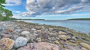 En klippig kustlinje med ett lugnt vattenområde och en skog i bakgrunden.