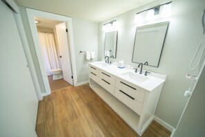 Un baño con tocador blanco, dos lavamanos, un espejo grande y cabina de ducha.