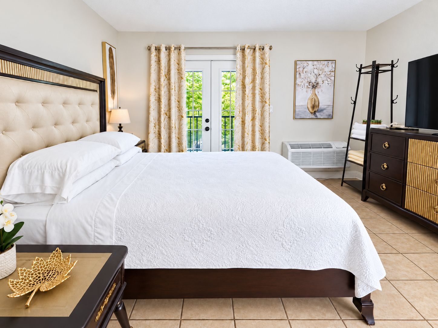 A hotel room with a large bed, a bedside table with a lamp, a dresser, and a window with curtains.
