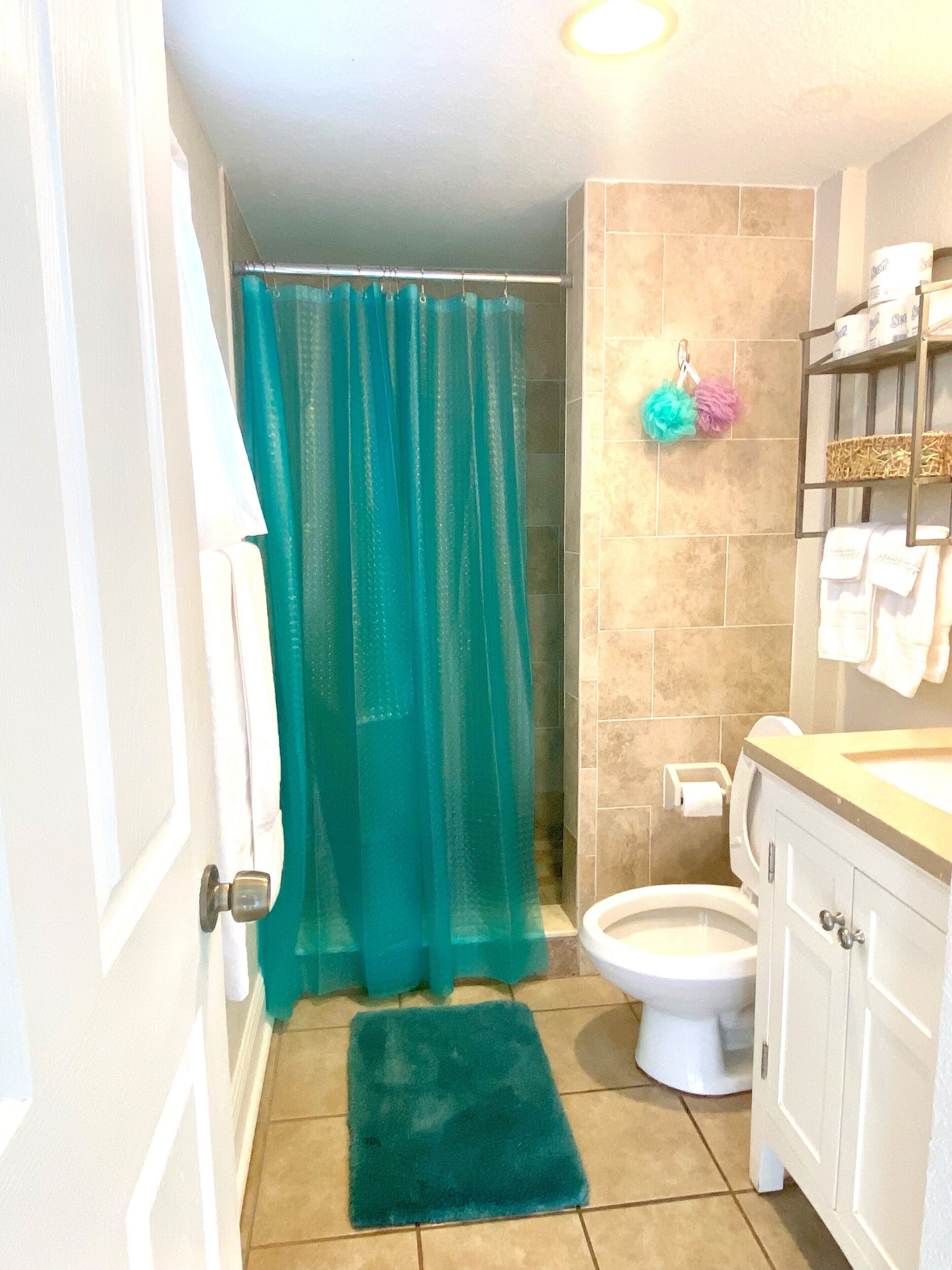 A bathroom with a shower curtain, a toilet, a sink, and a shelf with towels.