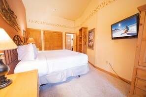 A bedroom with a large bed, wooden wardrobe, and a television on the wall. - Arapahoe Lodge 8105 (Keystone)