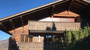 A two-story wooden chalet with a balcony, large windows, and a view of the surrounding landscape. - Halten (Hofmann) by Interhome (Zweisimmen)
