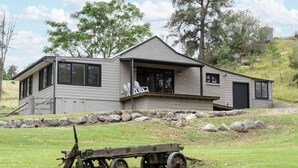 A two-story house with a balcony, large windows, and a stone wall in front. - The River Cottage - Idyllic river side cottage (Joadja)