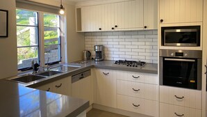 A modern kitchen with white cabinetry, a gas stove, an oven, a microwave, and a dishwasher. - The River Cottage - Idyllic river side cottage (Joadja)