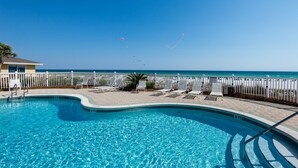 A swimming pool with a view of the ocean, surrounded by lounge chairs and a white fence. - Beautiful 4th FL Condo, Gulf Front, Seasonal Beach Service (Miramar Beach)