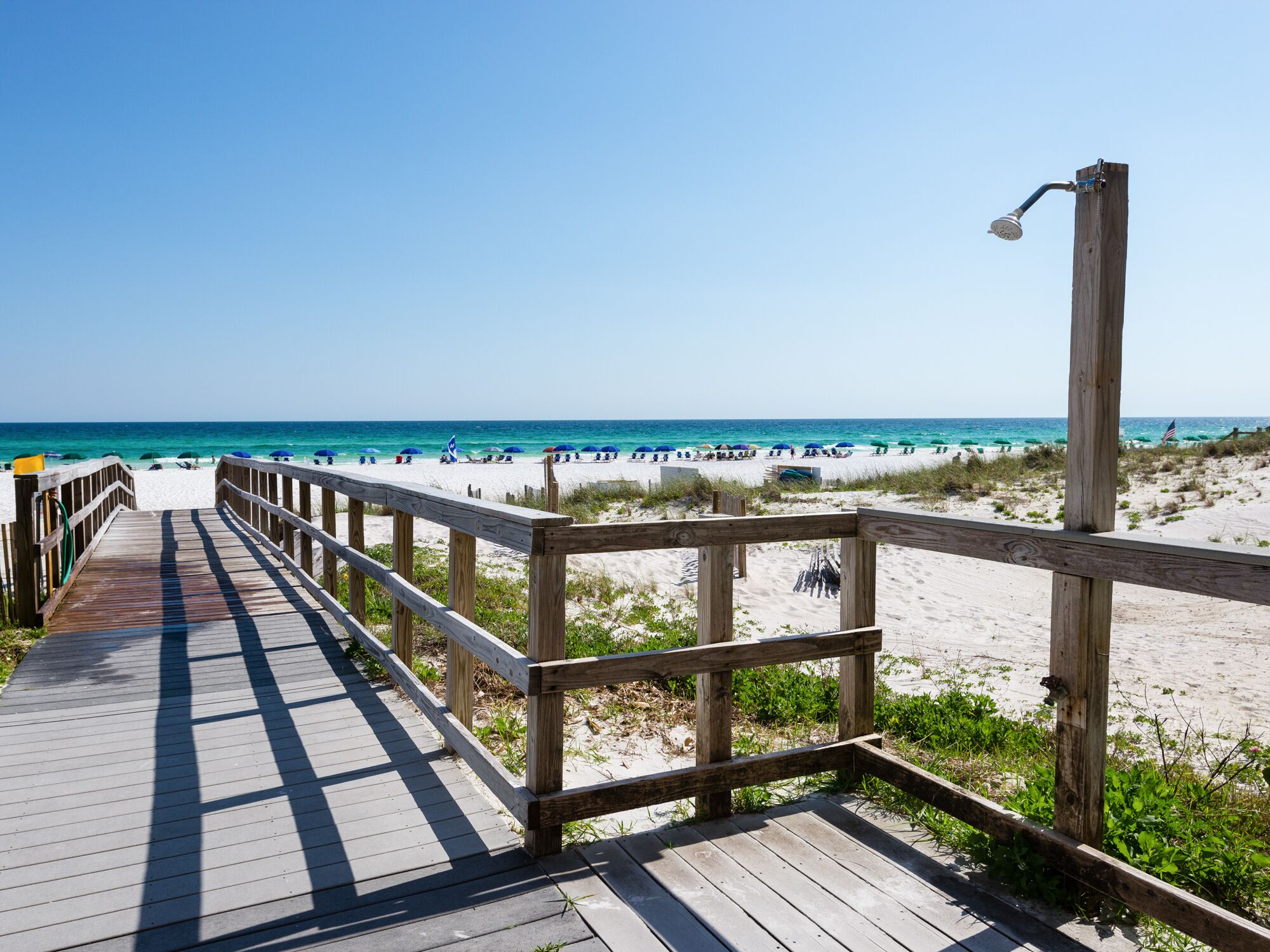A wooden boardwalk leading to a beach with umbrellas and a flag.