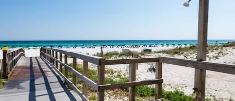A wooden boardwalk leading to a beach with umbrellas and a flag.