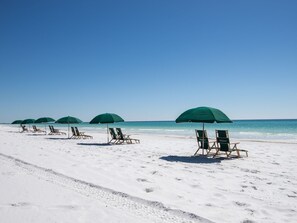 Una spiaggia con file di ombrelloni verdi e lettini di legno rivolti verso l'oceano.