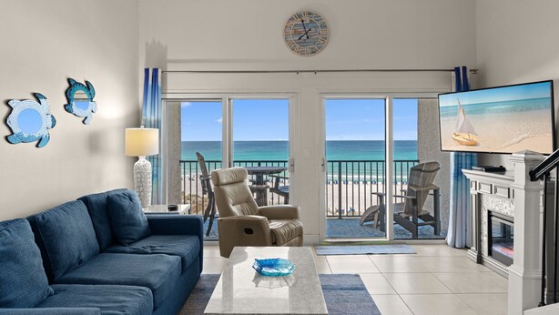A living room with a sofa, armchair, coffee table, TV, fireplace, and a view of the beach. - Beautiful 4th FL Condo, Gulf Front, Seasonal Beach Service (Miramar Beach)