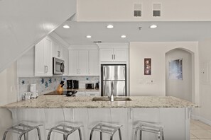 A modern kitchen with white cabinets, stainless steel appliances, and a marble countertop.
