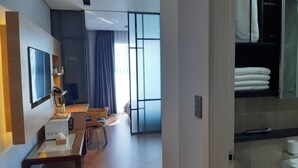 A modern hotel room with a wooden floor, a dining area with a table and chairs, a TV mounted on the wall, and a large window with curtains. - Sunrise Hotel Junior Suite room11F  (Sokcho-si)