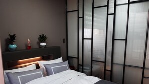 A modern bedroom with a bed, bedside tables, and a wall-mounted shelf with decorative items. - Sunrise Hotel Junior Suite room11F  (Sokcho-si)