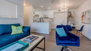 Een moderne woonkamer met een blauwe bank, een salontafel met boeken, en een eethoek met blauwe stoelen.
