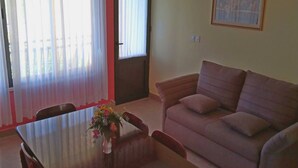 A living room with a sofa, a dining table with chairs, and a vase with flowers. - Apartment Kata - Two-Bedroom Apartment with Balcony and Garden View (Lumbarda)
