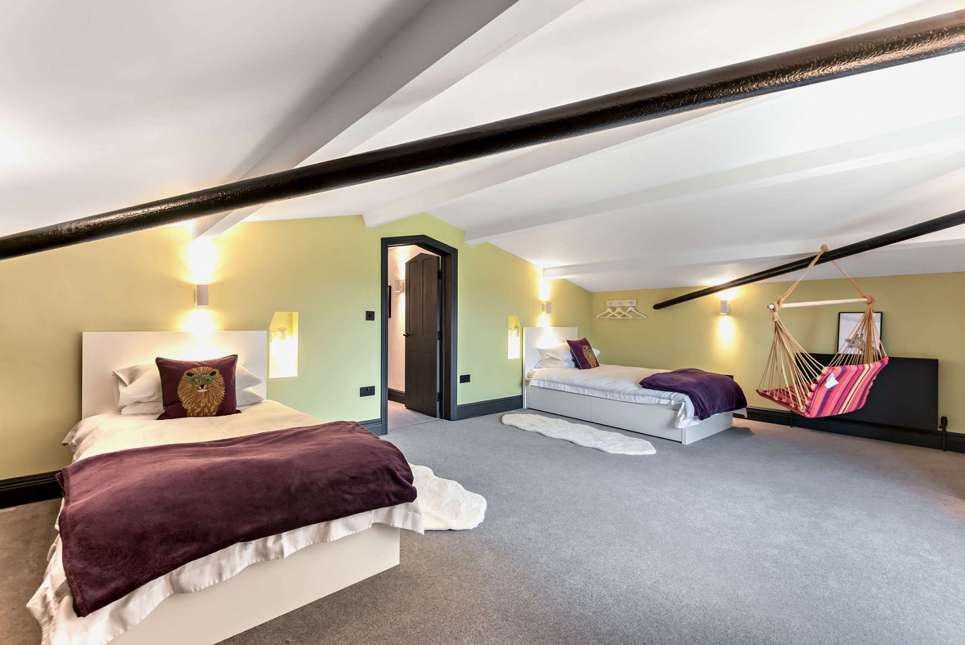 A spacious attic bedroom with two beds, a hanging chair, and a door leading to another room.