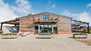 A modern building with a wooden facade, large glass windows, and a covered patio area with outdoor seating. - Large 6 bedroom luxury holiday home in the Cotswolds with a hot tub - Folly View (Faringdon)