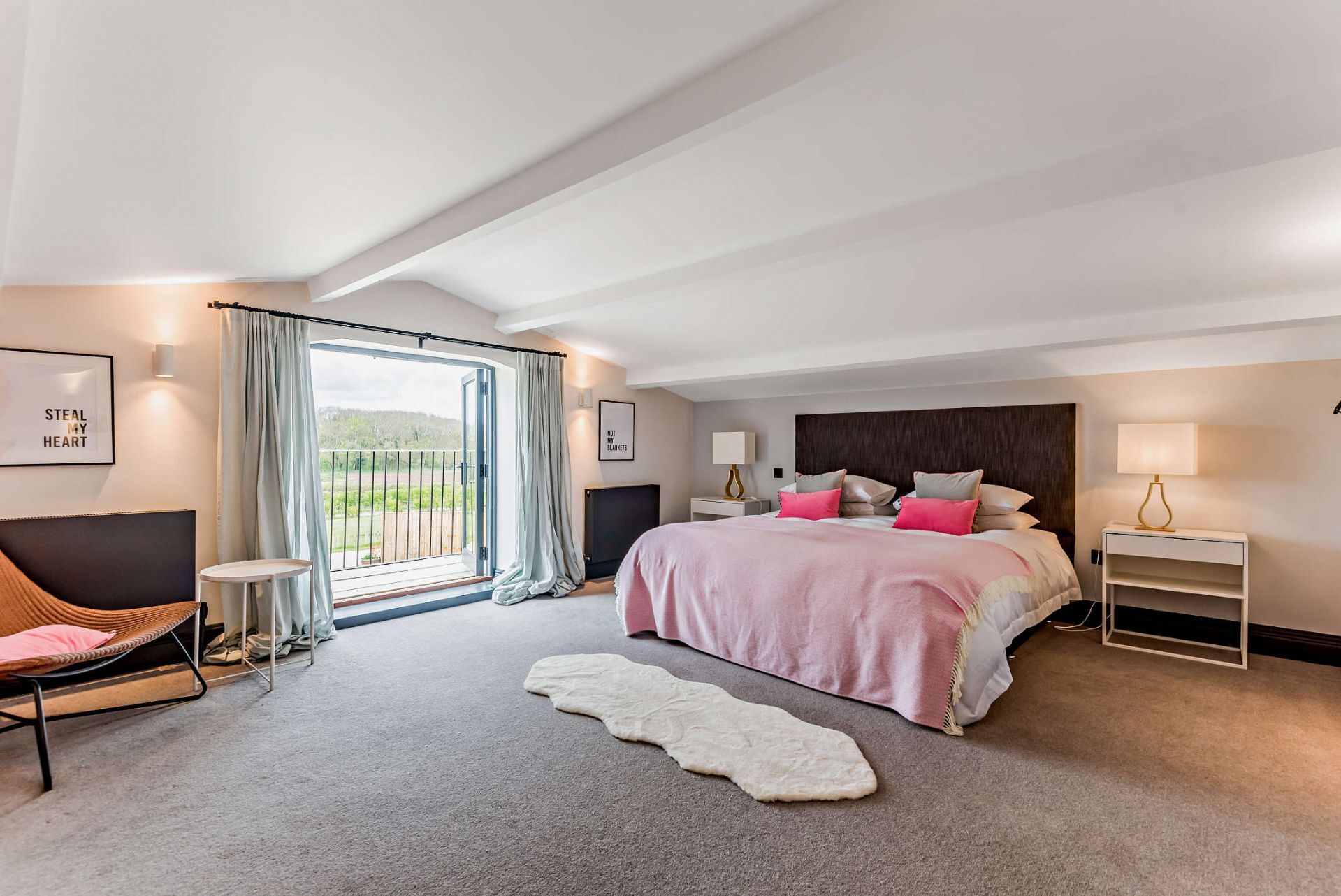 A modern bedroom with a large bed, a sofa, a small table, and a view of the outdoors.